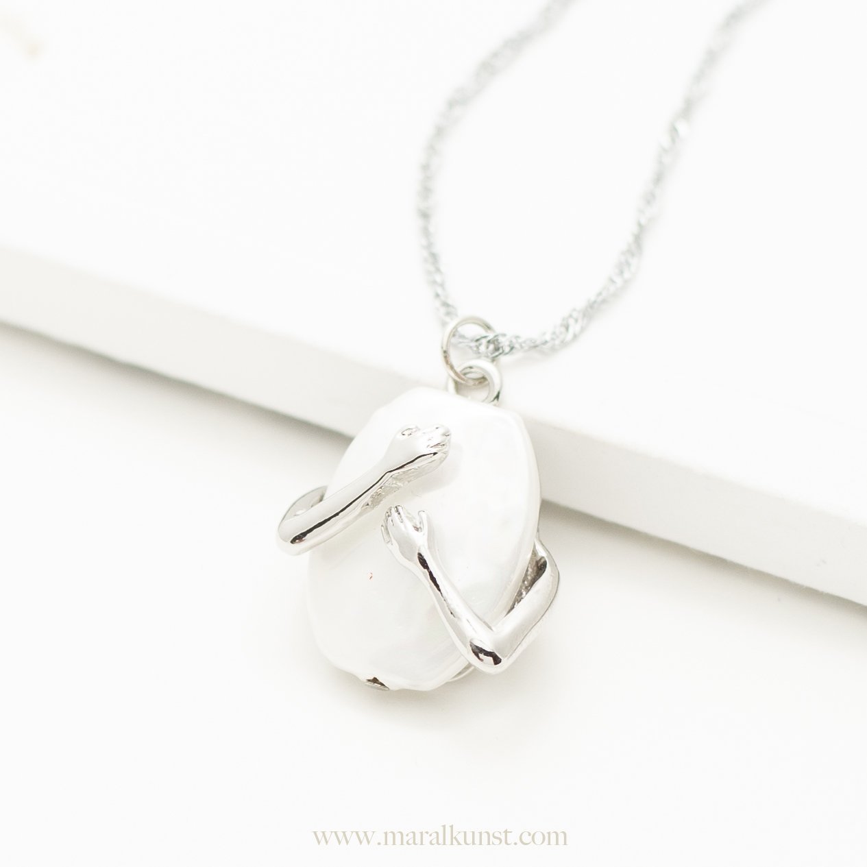 a necklace with shape of two hands hugging a pearl in the middle