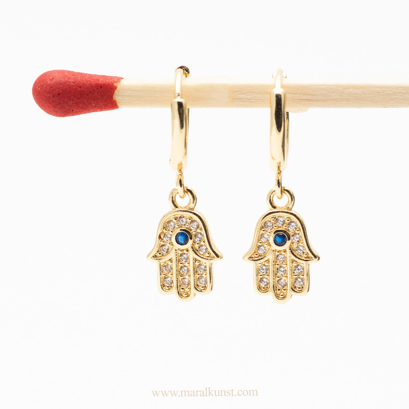 a pair of Fatima hand shape earrings are hanging on a matchstick 
