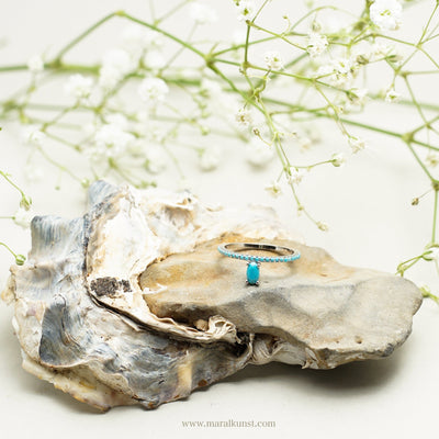 a turquoise ring in stainless steel is laying on the white table